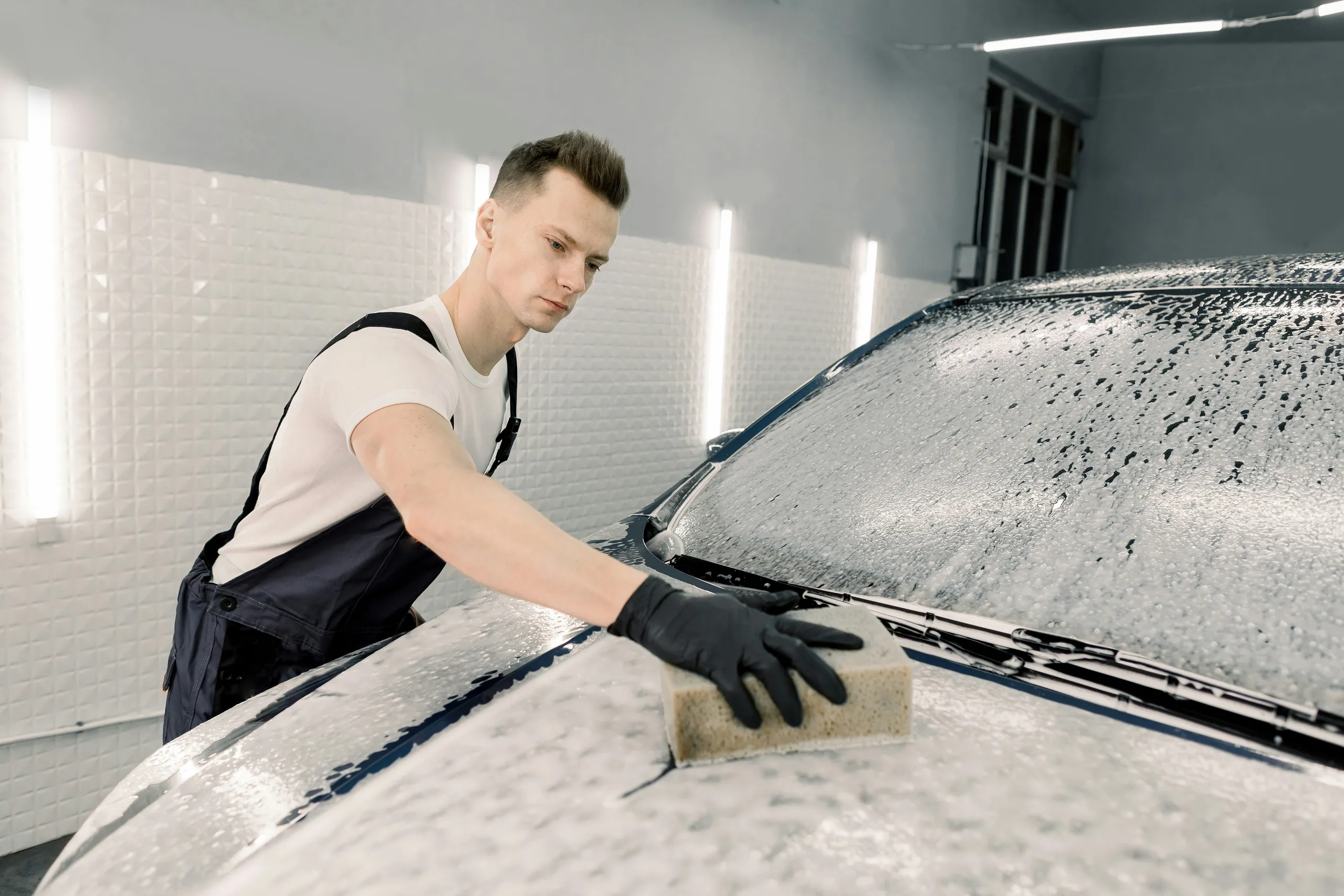 Un técnico lava con esponja enjabonada el capó del coche en el estudio de detailing